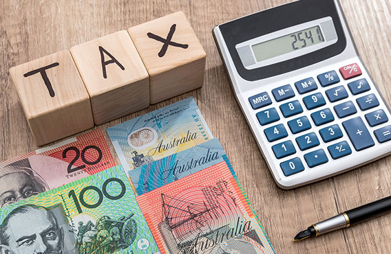 Blocks which spell out TAX, a calculator, pen and Australian money placed on a table