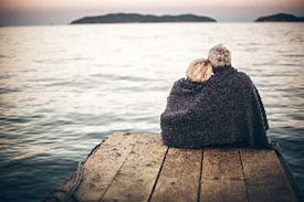 Senior couple sitting on the edge of a pier with a blanket around them