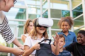 Excited group of children standing around little girl wearing goggles, while teacher assists