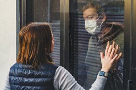 A man in a medical mask holds his hand to a woman through a window, practicing caremongering.