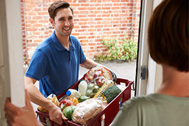 Man delivering box of fruit and vegetables to woman as part of food subscription service.
