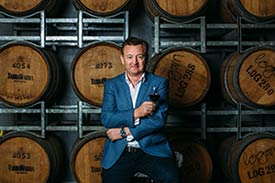 Picture of Luke Mangan standing in front of wine barrels with a glass of red wine