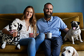 Happy teaching couple with their dogs relaxing on a couch, embodying the work-life balance supported by Teachers Mutual Bank's financial solutions for educators.