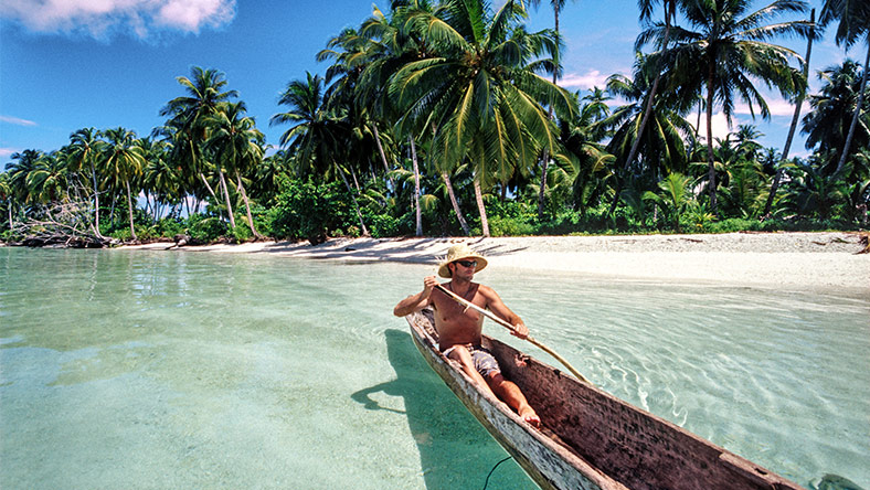 Man on holiday in Indonesia paddling in a long tail boat on a tropical beach.