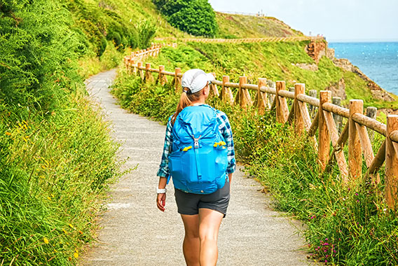 A woman hiking in warm weather near the coast with a blue backpack and cap