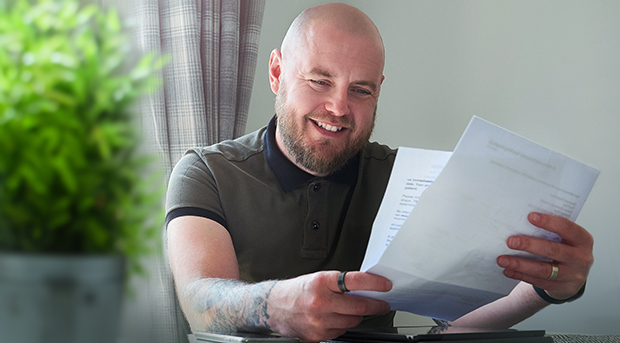 A man sits at his kitchen table looking happily at his home loan documents.