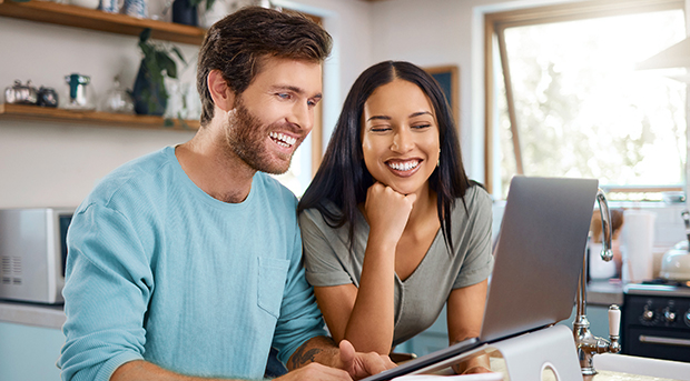 A couple at their kitchen table look happily at their home loan application on a laptop.